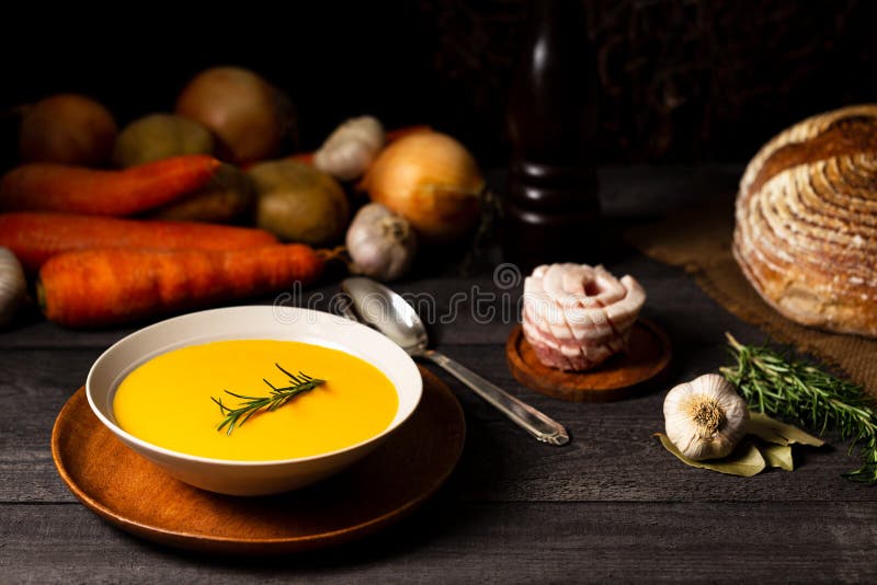 Carrot and potato soup with rosemary twig on a grey wood table with a spoon, onion, potatoes, carrot, garlic, bread loaf, pork royalty free stock photos Carrot and potato soup with rosemary twig on a grey wood table with a spoon, onion, potatoes, carrot, garlic, bread loaf, pork royalty free stock photos