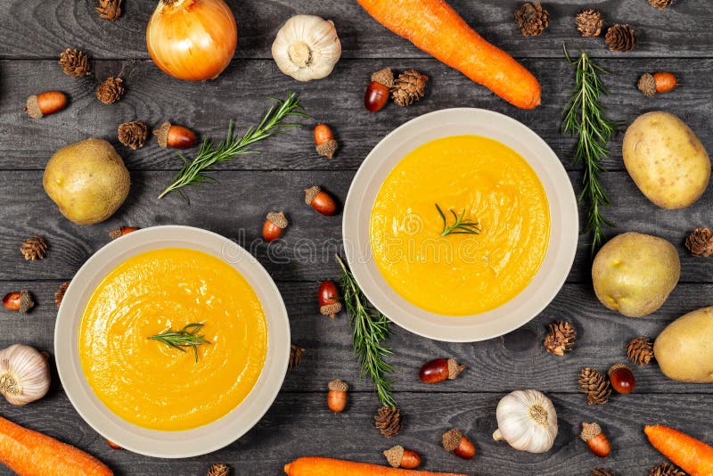 Carrot and potato soup bowls on a black wood table with vegetables, acorns, pine cones, garlic and rosemary. Flat lay stock photos Carrot and potato soup bowls on a black wood table with vegetables, acorns, pine cones, garlic and rosemary. Flat lay stock photos