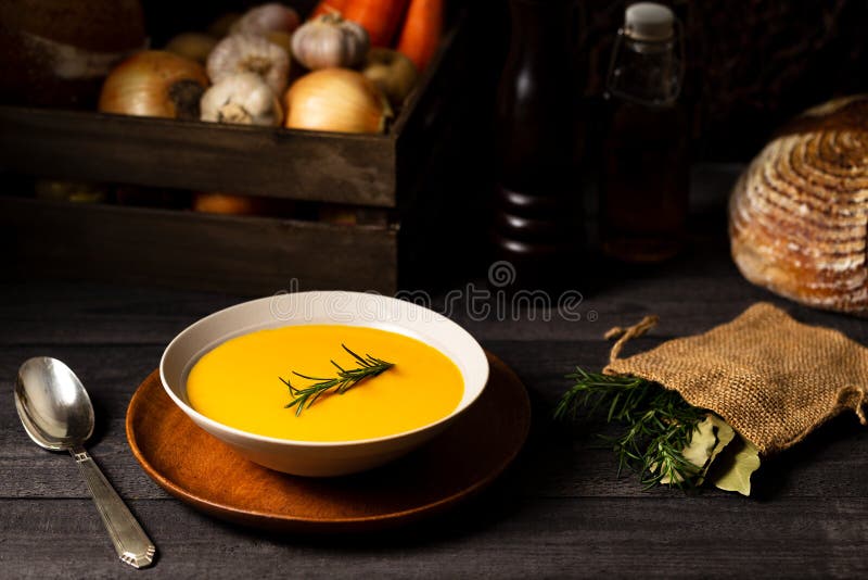 Carrot and potato soup with rosemary twig in a bowl with a vintage silver spoon on a grey wood table with a crate of vegetables royalty free stock images Carrot and potato soup with rosemary twig in a bowl with a vintage silver spoon on a grey wood table with a crate of vegetables royalty free stock images