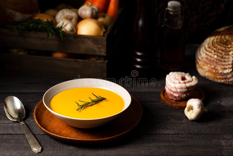 Carrot and potato soup with rosemary twig in a bowl with a vintage silver spoon on a grey wood table with a crate of vegetables stock photography Carrot and potato soup with rosemary twig in a bowl with a vintage silver spoon on a grey wood table with a crate of vegetables stock photography
