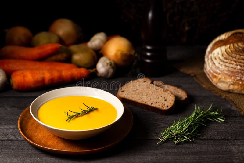 Carrot and potato soup with rosemary twig on a grey wood table, alongside onions, potatoes, carrots, bread loaf, and rosemary royalty free stock photo Carrot and potato soup with rosemary twig on a grey wood table, alongside onions, potatoes, carrots, bread loaf, and rosemary royalty free stock photo