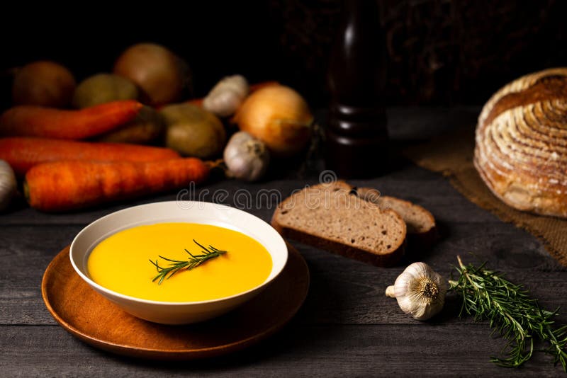 Carrot and potato soup with rosemary twig on a grey wood table, alongside onions, potatoes, carrots, garlic, bread loaf. royalty free stock images Carrot and potato soup with rosemary twig on a grey wood table, alongside onions, potatoes, carrots, garlic, bread loaf. royalty free stock images