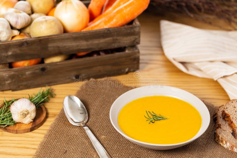 Carrot and potato soup on a wood table with vegetables in a crate alongside bread, silver spoon, napkin, garlic and rosemary stock images Carrot and potato soup on a wood table with vegetables in a crate alongside bread, silver spoon, napkin, garlic and rosemary stock images
