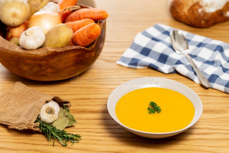Carrot and potato soup on a wood table with vegetables in a wooden bowl alongside bread, silver spoon, napkin, laurel, garlic stock photos Carrot and potato soup on a wood table with vegetables in a wooden bowl alongside bread, silver spoon, napkin, laurel, garlic stock photos