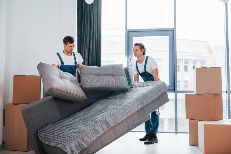 Carrying Heavy Sofa. Two Young Movers in Blue Uniform Working Indoors ...