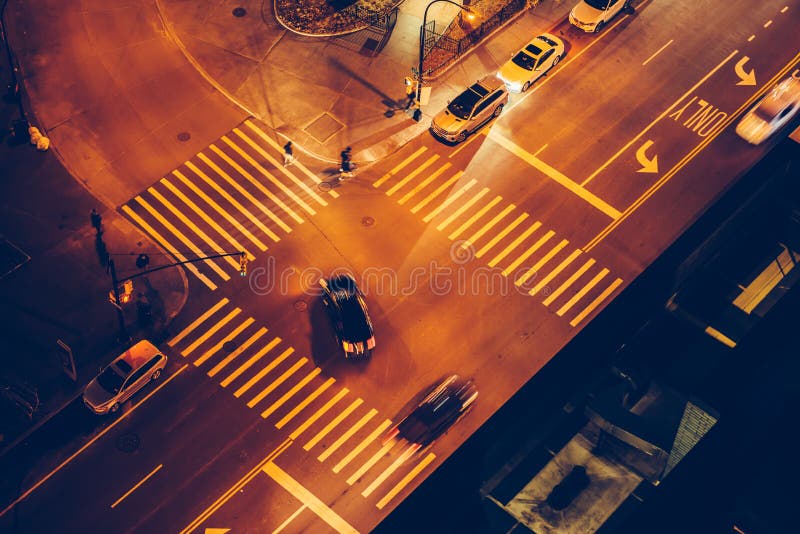Cars and people on road intersection with signal lights and crosswalks at night time in the city street.