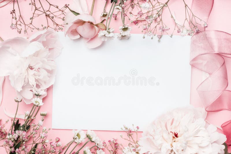 Carta in bianco bianca con i fiori pastelli e nastro su fondo pallido rosa, struttura floreale Saluto creativo, invito