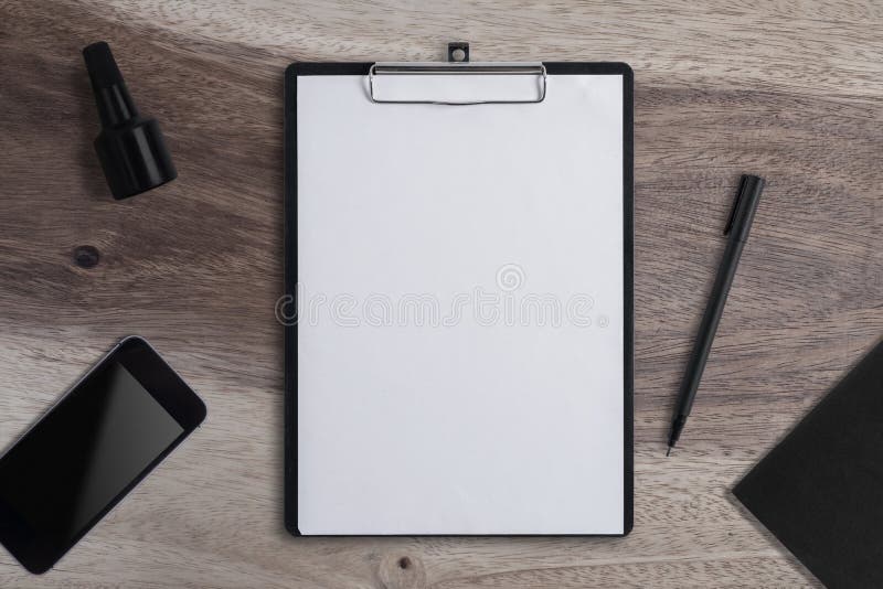 Carta in bianco sulla lavagna per appunti con il telefono e penna sul fondo di legno della tavola immagine stock Carta in bianco sulla lavagna per appunti con il telefono e penna sul fondo di legno della tavola immagine stock