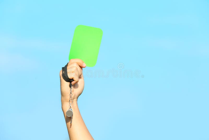 Carta verde di rappresentazione dell'arbitro di calcio contro cielo blu immagini stock Carta verde di rappresentazione dell'arbitro di calcio contro cielo blu immagini stock
