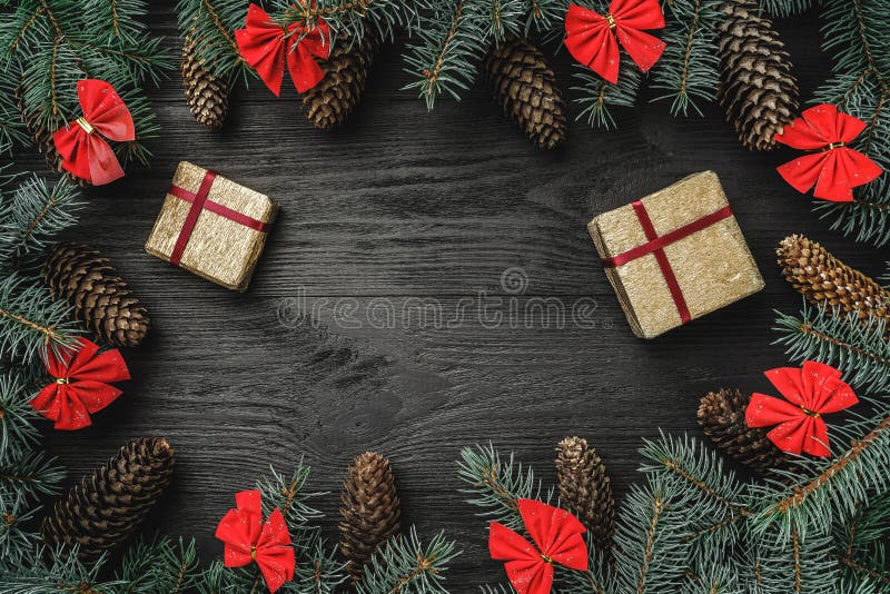 Cartão do Xmas O abeto ramifica com cones e as bacias vermelhas, no fundo de madeira preto Weihnachtspakete - presente de Natal