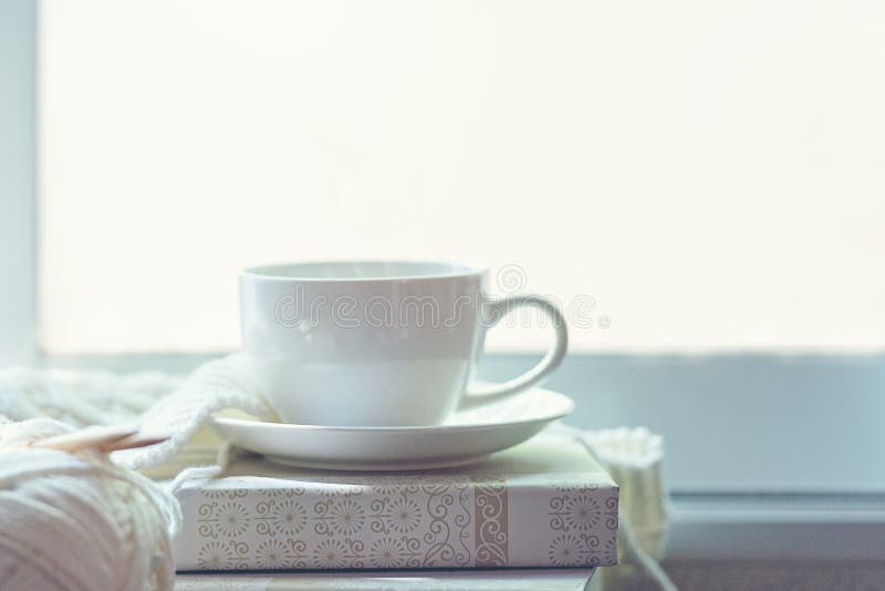 Casa accogliente di inverno del caffè con i maglioni e la palla tricottati caldi di filato vicino al davanzale, tazza della caram