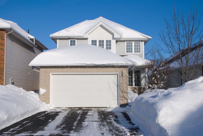 Contemporary 2 floor beige brick house with garage in front; heavy snow; driveway in foreground; frontal view; deep blue sky. Contemporary 2 floor beige brick house with garage in front; heavy snow; driveway in foreground; frontal view; deep blue sky