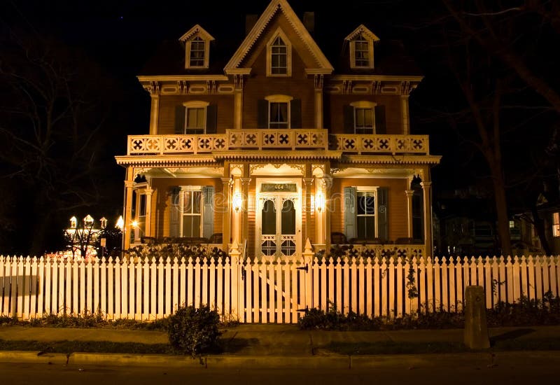 A somewhat spooky night view of a Victorian era house with a white picket fence in the foreground. A somewhat spooky night view of a Victorian era house with a white picket fence in the foreground.