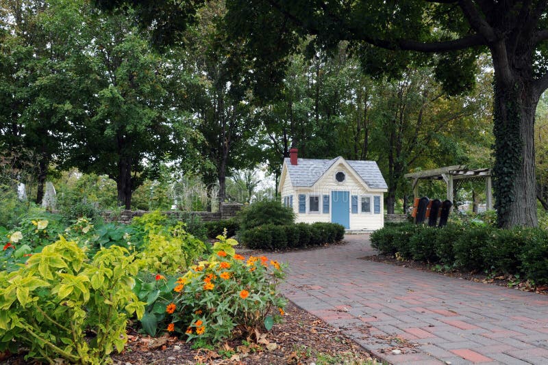 A tiny house at the end of a brick walkway, surrounded by trees, shrubs and flowers. A tiny house at the end of a brick walkway, surrounded by trees, shrubs and flowers.