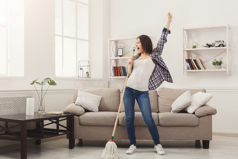 Happy woman cleaning home, singing at mop like at microphone and having fun, copy space. Housework, chores concept. Happy woman cleaning home, singing at mop like at microphone and having fun, copy space. Housework, chores concept