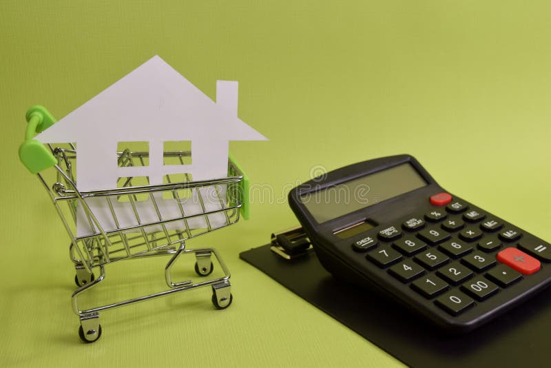 A casa pôs em um carrinho de compras e em uma calculadora sobre a mesa Economias para a casa, casas de compra, casas da venda, be foto de stock royalty free A casa pôs em um carrinho de compras e em uma calculadora sobre a mesa Economias para a casa, casas de compra, casas da venda, be foto de stock royalty free