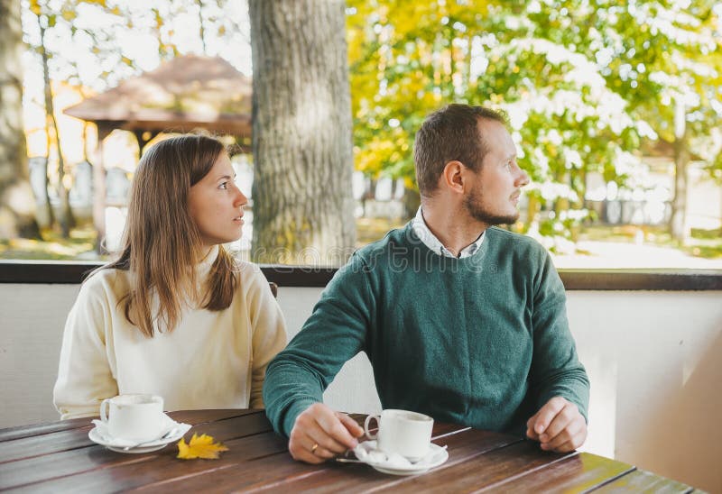 Casal bonito olhando de lado enquanto tomava café da manhã e bebe chá no jardim de outono fotografia de stock Casal bonito olhando de lado enquanto tomava café da manhã e bebe chá no jardim de outono fotografia de stock