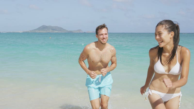 Casal feliz se divertindo na praia correndo na água