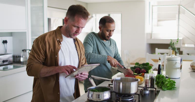 Casal homossexual multi-étnico preparando comida na cozinha um usando tablet