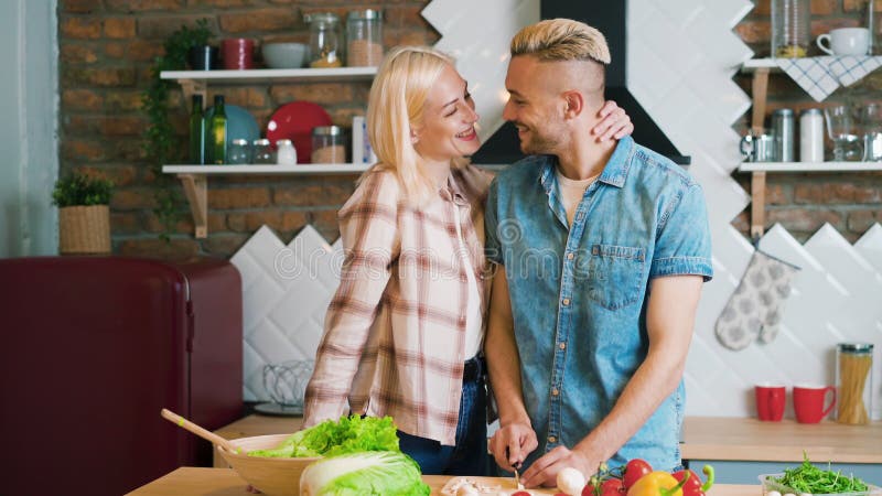 Casal jovem beijando e cozinhando juntos refeições vegetarianas na cozinha em casa