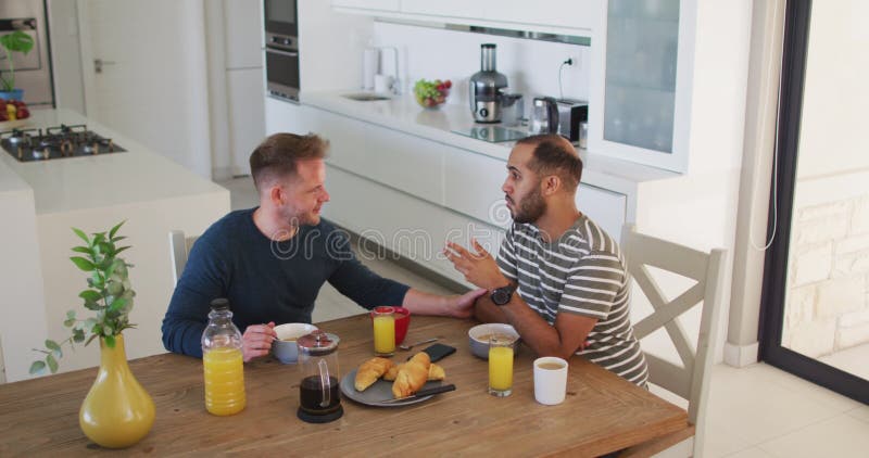 Casal macho homossexual multi-étnico sentado tomando café da manhã e conversando