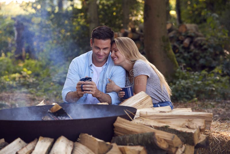 Casal romântico acampando sentado por fogueira em uma tigela de fogo com bebidas quentes