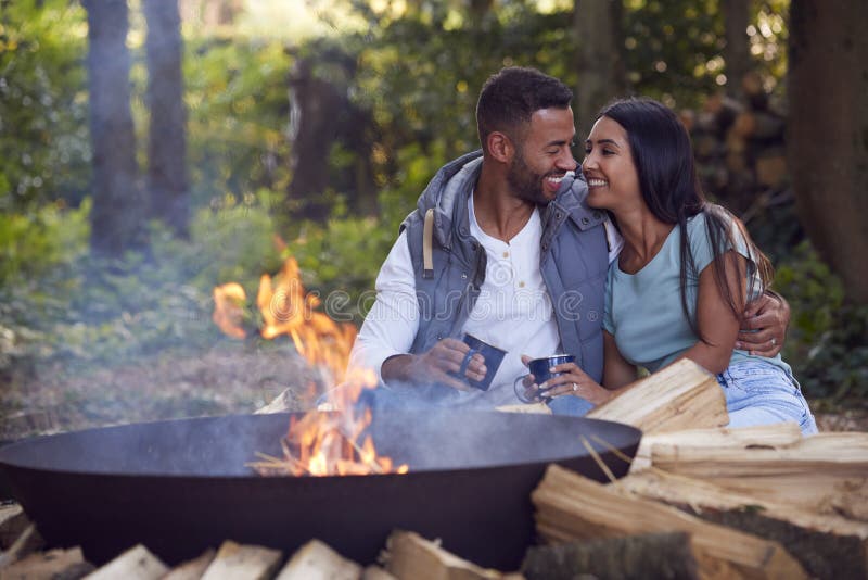 Casal romântico acampando sentado por fogueira em uma tigela de fogo com bebidas quentes