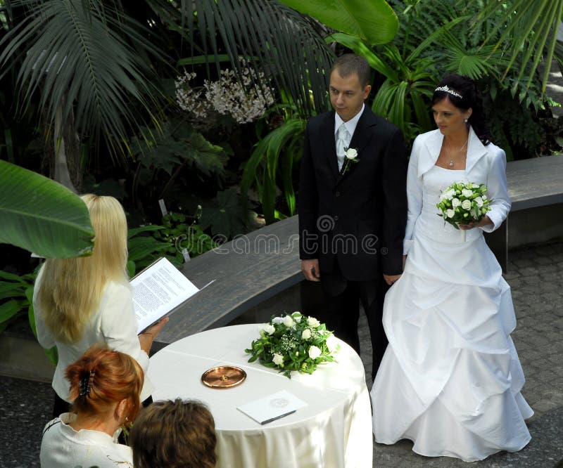 A young couple standing in a garden setting before a female officiant. A young couple standing in a garden setting before a female officiant.