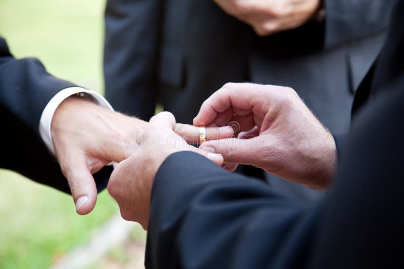 One groom placing the ring on another man's finger during gay wedding. One groom placing the ring on another man's finger during gay wedding.