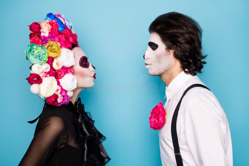 Casal assustador morto celebra o halloween juntos, organiza festa à fantasia,  usa trajes mexicanos tradicionais, maquiagem vívida, coroa de flores  vermelha, pose no estúdio, fica ombro a ombro. dia da morte