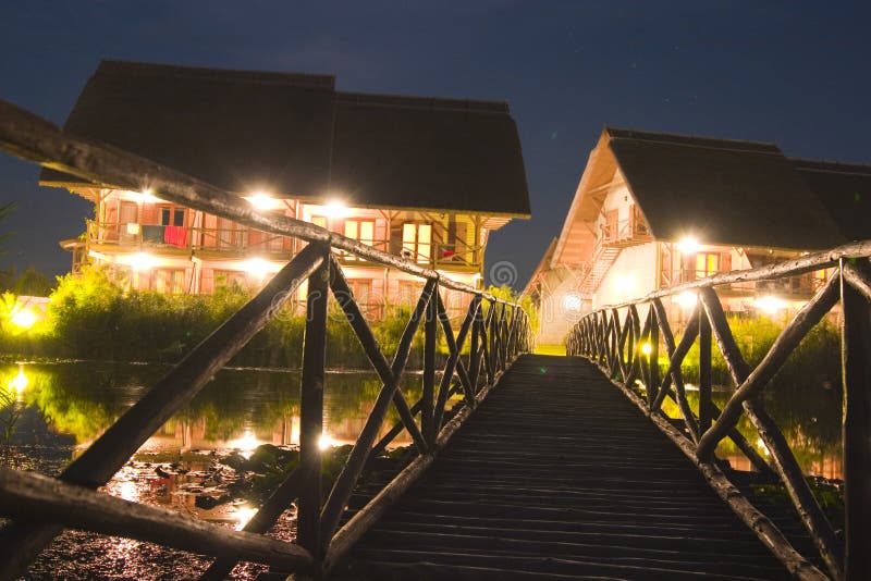 Two cottage houses seen across a small wooden bridge, nighttime. Two cottage houses seen across a small wooden bridge, nighttime.