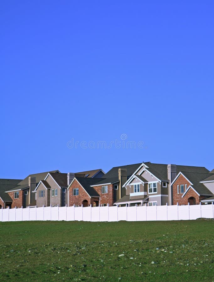 Row of newly built single-family houses behind a white fence with lots of blue sky and green grass. Row of newly built single-family houses behind a white fence with lots of blue sky and green grass