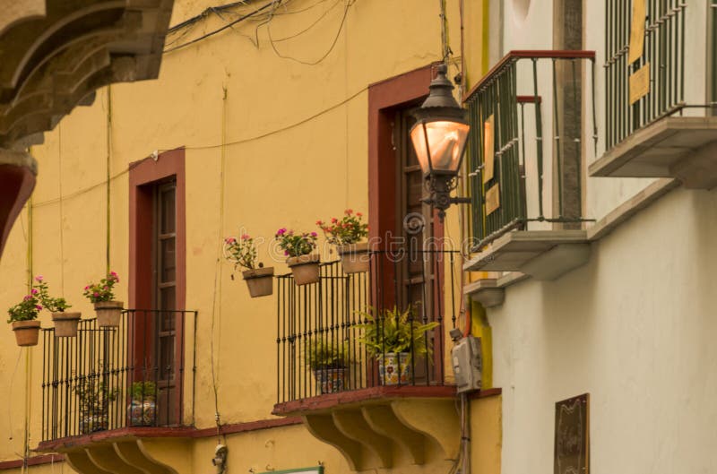 Casas típicas de Guanajuato, México. Vista exterior de janelas da construção com as flores em pasta que penduram das bordas de balcões do ferro forjado em Guanajuato histórico do centro, México, um local do patrimônio mundial do UNESCO