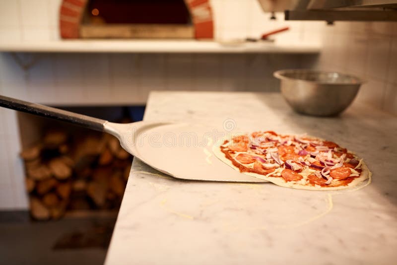 Food, italian kitchen, culinary, baking and cooking concept - peel taking pizza off table at pizzeria. Food, italian kitchen, culinary, baking and cooking concept - peel taking pizza off table at pizzeria