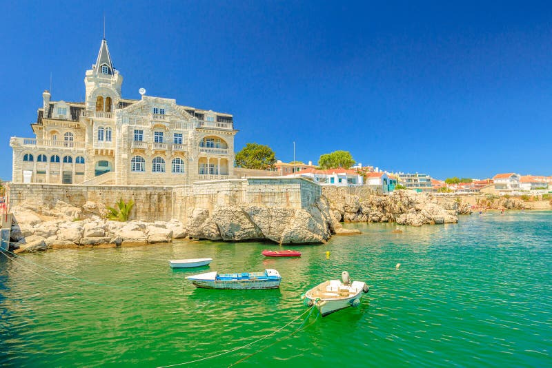 Scenic landscape of abandoned Palace Seixas and boats on the waterfront of Cascais, Lisbon Coast in Portugal. Praia da Rainha on the distance. Turquoise sea in summertime. Copy space with blue sky. Scenic landscape of abandoned Palace Seixas and boats on the waterfront of Cascais, Lisbon Coast in Portugal. Praia da Rainha on the distance. Turquoise sea in summertime. Copy space with blue sky.