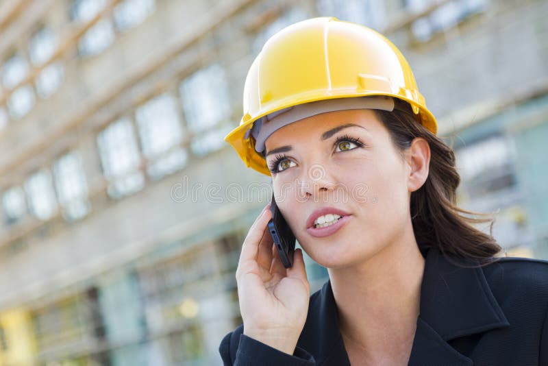 Casco d'uso del giovane appaltatore femminile sul sito facendo uso del telefono immagini stock Casco d'uso del giovane appaltatore femminile sul sito facendo uso del telefono immagini stock