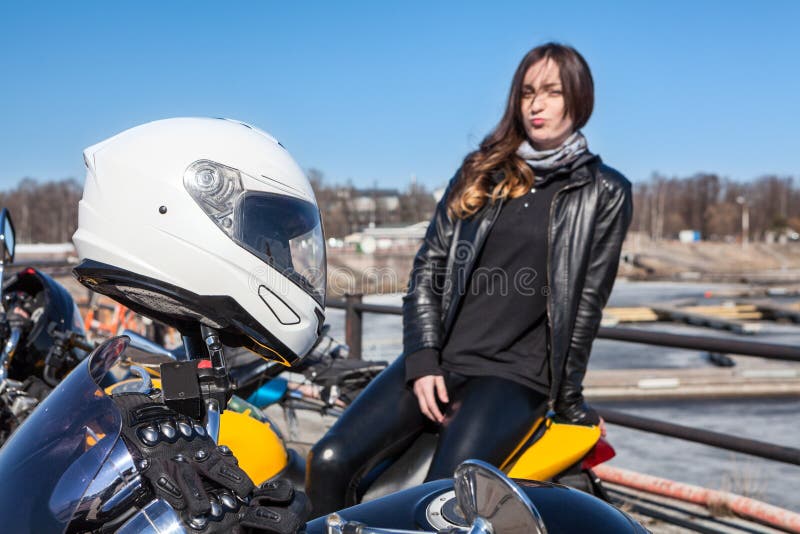 Casco protector blanco en los manillares de la motocicleta y pasajero de la mujer no en foco en fondo imágenes de archivo libres de regalías Casco protector blanco en los manillares de la motocicleta y pasajero de la mujer no en foco en fondo imágenes de archivo libres de regalías