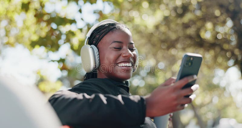 Casque fitness et femme noire avec téléphone dans le parc pour l'exercice et l'entraînement. Joyeux relax et personne rire banque de vidéos