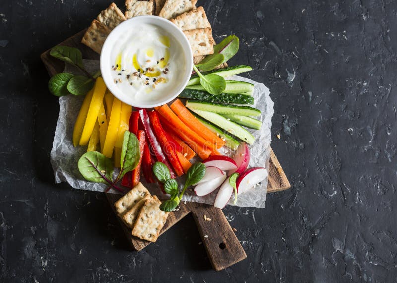 Casse-croûte sain - les légumes crus et le yaourt sauce sur une planche à découper en bois, sur un fond foncé, vue supérieure Nou image stock Casse-croûte sain - les légumes crus et le yaourt sauce sur une planche à découper en bois, sur un fond foncé, vue supérieure Nou image stock