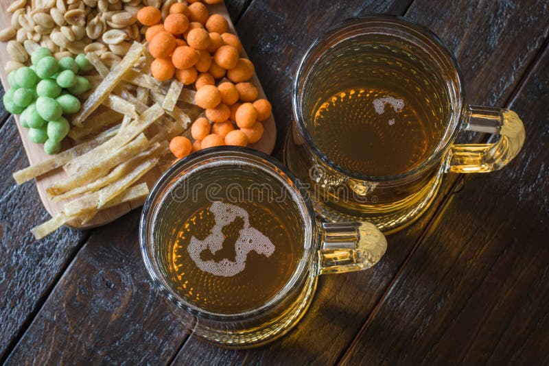 Casse-croûte dans la bière et deux tasses de bière blonde, sur une table en bois, dans une barre Arachides, arachides dans une co images stock Casse-croûte dans la bière et deux tasses de bière blonde, sur une table en bois, dans une barre Arachides, arachides dans une co images stock