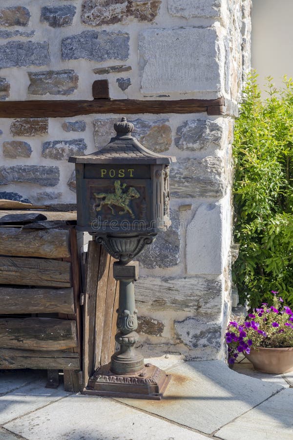 An old, metal mailbox on a stand stands against a stone wall on a village street close-up. An old, metal mailbox on a stand stands against a stone wall on a village street close-up