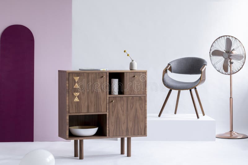 Cassettone di legno alla moda accanto alla sedia grigia sulla piattaforma bianca nell'interno d'avanguardia fotografia stock libera da diritti
