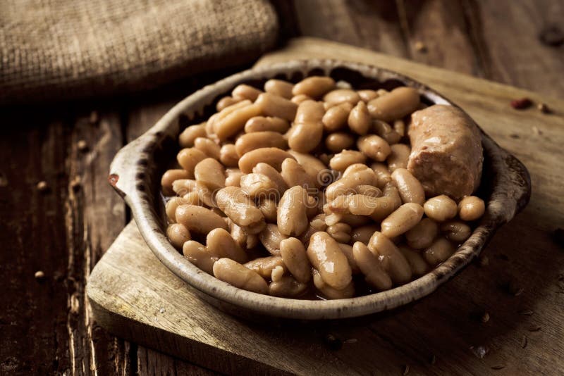 Closeup of an earthenware bowl with a cassoulet de Castelnaudary, a typical bean stew from Occitanie, in France, on a rustic wooden table. Closeup of an earthenware bowl with a cassoulet de Castelnaudary, a typical bean stew from Occitanie, in France, on a rustic wooden table