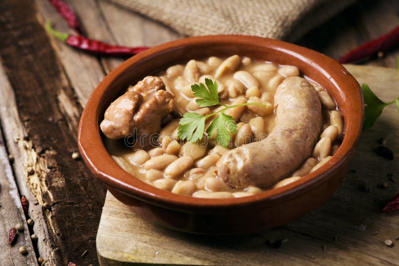 Closeup of an earthenware bowl with a cassoulet de Castelnaudary, a typical bean stew from Occitanie, in France, on a rustic wooden table. Closeup of an earthenware bowl with a cassoulet de Castelnaudary, a typical bean stew from Occitanie, in France, on a rustic wooden table