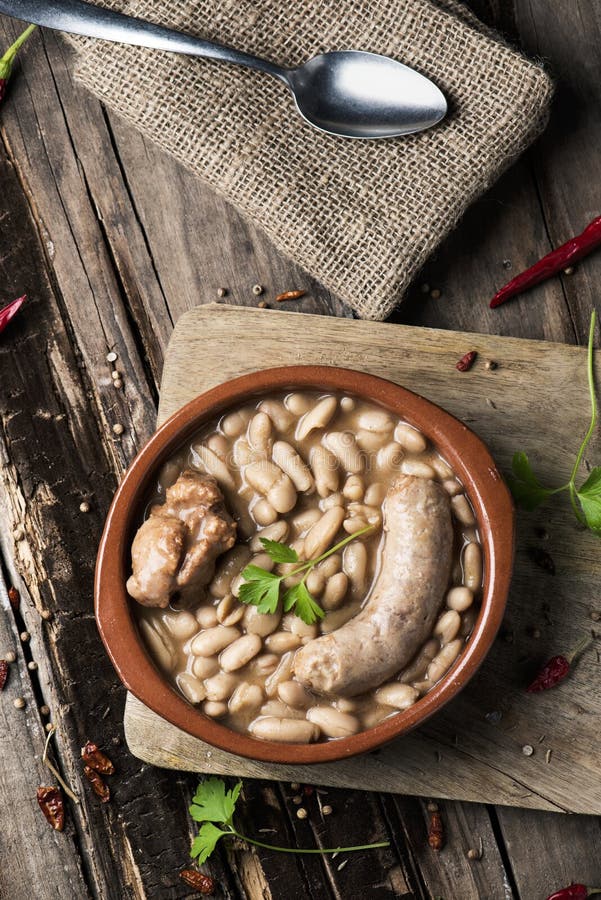 High-angle shot of an earthenware bowl with a cassoulet de Castelnaudary, a typical bean stew from Occitanie, in France, on a rustic wooden table. High-angle shot of an earthenware bowl with a cassoulet de Castelnaudary, a typical bean stew from Occitanie, in France, on a rustic wooden table