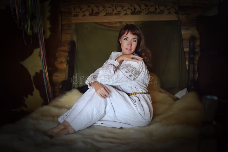 Castana in camicia antiquata di tela bianca con ricamo si siede su un letto medievale fotografie stock libere da diritti Castana in camicia antiquata di tela bianca con ricamo si siede su un letto medievale fotografie stock libere da diritti