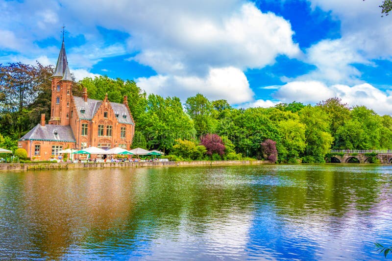 Minnewater castle with people enjoying the view at the outdoor restaurant seating by the Lake of Love in Bruges, Belgium, fairytale scenery in Bruges. Bruges Brugge historic city is a prominent World Heritage Site of UNESCO.August 7th 2016. Minnewater castle with people enjoying the view at the outdoor restaurant seating by the Lake of Love in Bruges, Belgium, fairytale scenery in Bruges. Bruges Brugge historic city is a prominent World Heritage Site of UNESCO.August 7th 2016