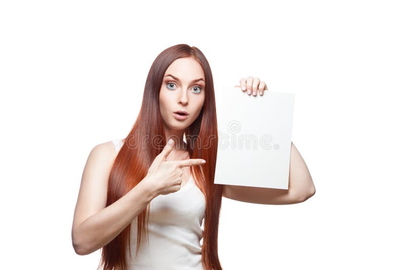 Horizontal studio portrait of young attractive green-eyed caucasian female with long natural straight red hair which dressed in casual outfit. girl holding blank white cardboard sign by her left hand and pointing on sign with index finger of her right hand with funny expression on her face. isolated on white background, professional makeup, hairstyle and retouching. Horizontal studio portrait of young attractive green-eyed caucasian female with long natural straight red hair which dressed in casual outfit. girl holding blank white cardboard sign by her left hand and pointing on sign with index finger of her right hand with funny expression on her face. isolated on white background, professional makeup, hairstyle and retouching.