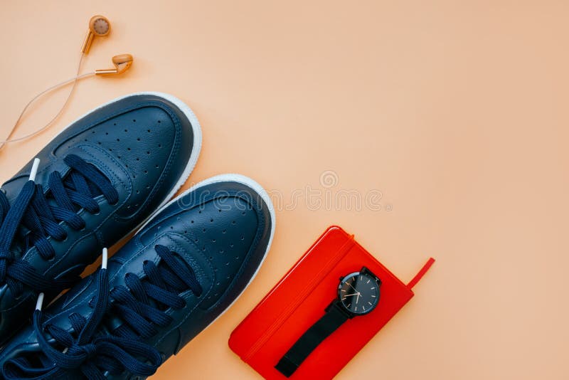 Casual flatlay with sneakers. Kiev, Ukraine - March 10, 2018: Flatlay of casual style dark blue leather sneakers with rose gold earphones, red notebook, black stock photo Casual flatlay with sneakers. Kiev, Ukraine - March 10, 2018: Flatlay of casual style dark blue leather sneakers with rose gold earphones, red notebook, black stock photo