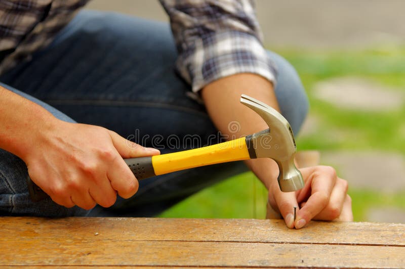 Casual man hammering nail in plank at home